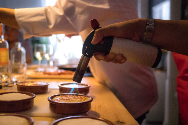 Alumno en clase de cocina flambeando el azúcar de una crema catalana con un soplete